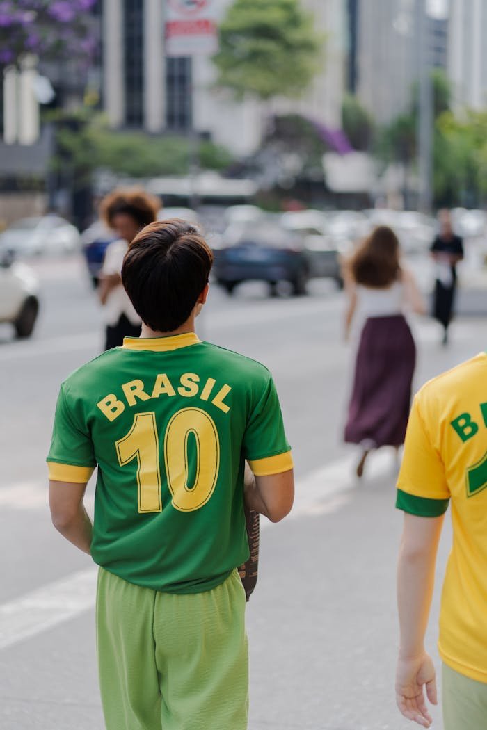 Adults in Brazil team shirts stroll through a bustling city street, showcasing vibrant urban life.